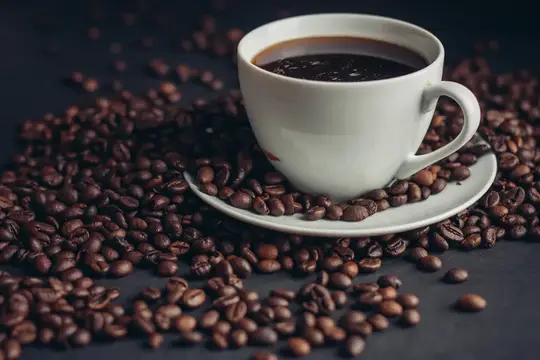 Белая чашка кофе на блюдце среди рассыпанных кофейных зёрен