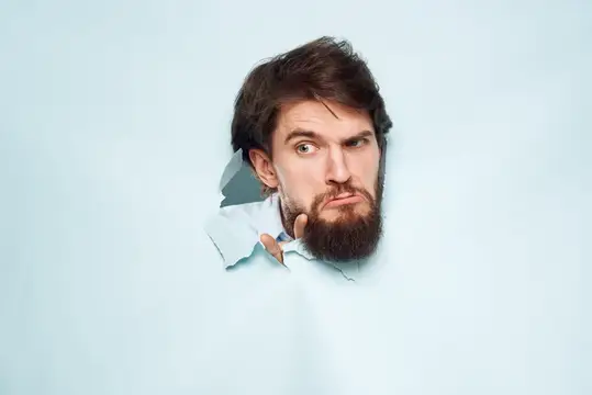 Бородатый мужчина, офисный менеджер, выражает недовольство на лице