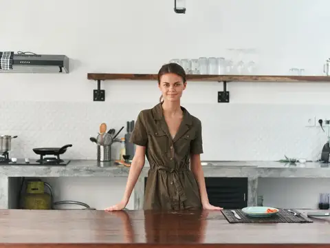 Женщина дома улыбается, стоит на кухне возле деревянного стола