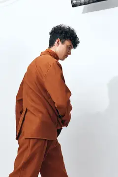 Серьезный, задумчивый студент с кудрявыми волосами сидит на бежевом фоне в студии