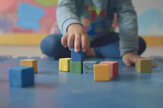 Ребёнок играет с цветными деревянными кубиками на полу