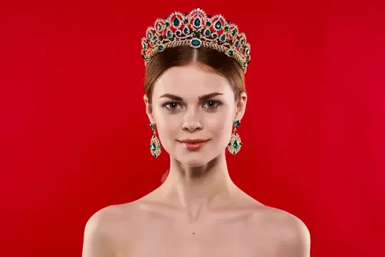 Молодая женщина в роскошной короне с изумрудами на красном фоне