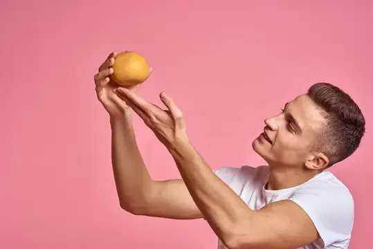 Молодой мужчина ловит апельсин на розовом фоне