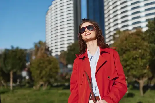 Улыбающаяся девушка в красном плаще и солнцезащитных очках на фоне высоток