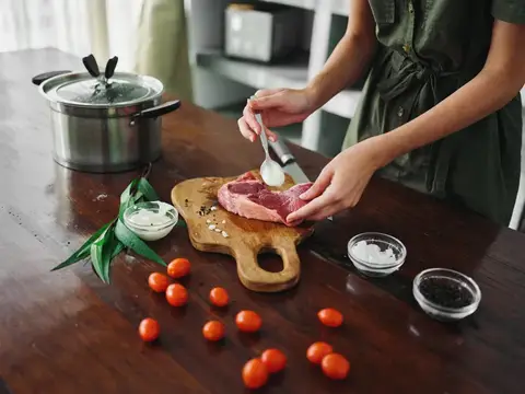 Женщина смазывает кусок мяса на кухонной доске