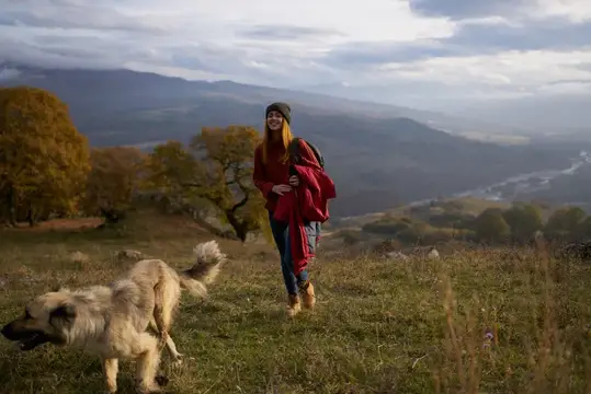 Улыбающаяся девушка с собакой гуляет по осенним холмам