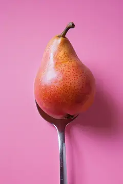Спелая груша на металлической ложке на розовом фоне