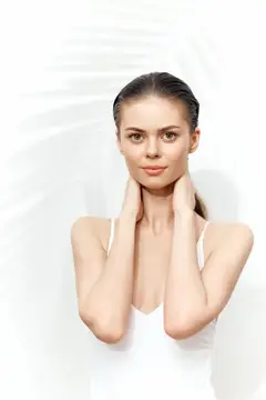 Молодая женщина с гладкой кожей держит руки у шеи на белом фоне