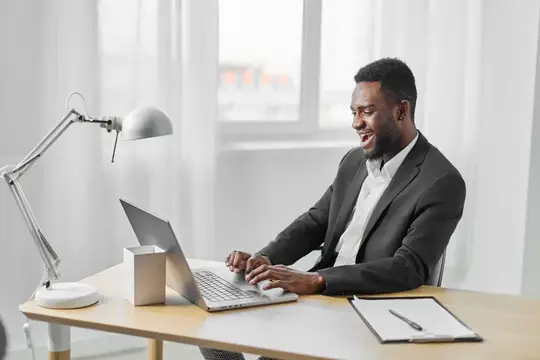 Улыбающийся темнокожий мужчина в костюме работает за ноутбуком в офисе