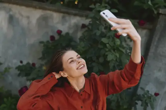 Улыбающаяся девушка в красной рубашке делает селфи на фоне роз