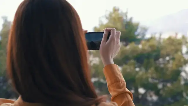 Девушка со спины фотографирует на смартфон горный пейзаж