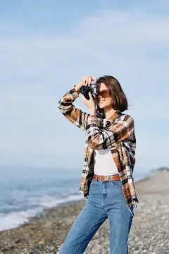 Молодая женщина в клетчатой рубашке фотографирует на берегу моря