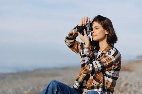 Молодая женщина в клетчатой рубашке фотографирует на плёночную камеру