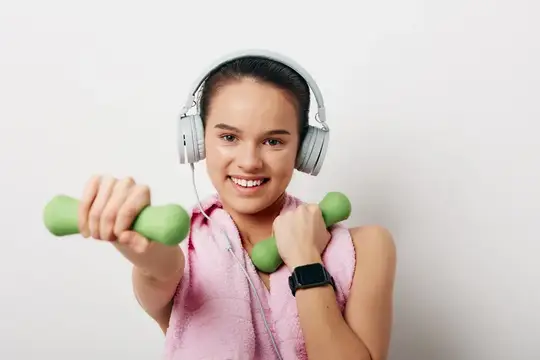 Улыбающаяся девушка с гантелями и в наушниках на тренировке