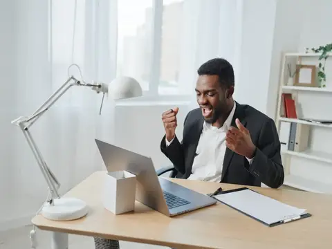 Радостный темнокожий мужчина в костюме празднует успех за ноутбуком