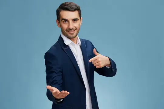 Веселый мужчина в деловом костюме указывает пальцем на свою ладонь и смотрит в камеру на синем фоне с копировальным пространством