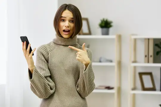 Удивлённая девушка с телефоном указывает на экран пальцем