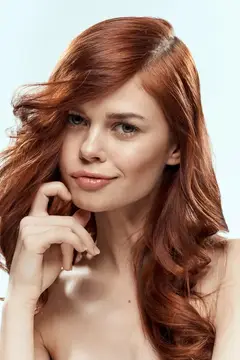Рыжеволосая девушка с мягкой улыбкой касается рукой лица