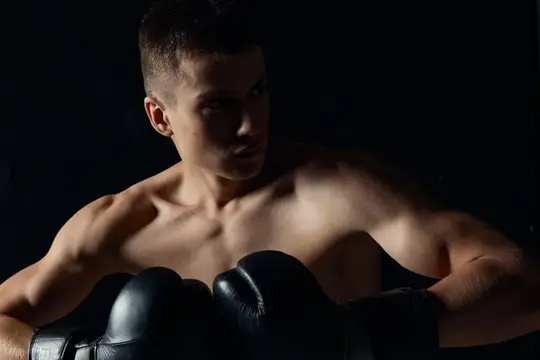Крупный план спортсмена в боксерских перчатках на черном фоне, кадрированное изображение