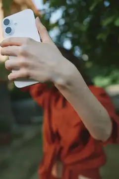 Рука человека в красной футболке держит белый смартфон на улице