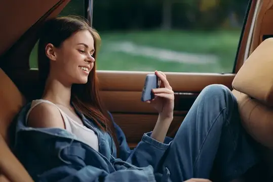 Улыбающаяся девушка с телефоном сидит в салоне автомобиля
