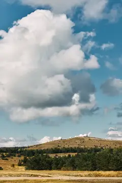 Огромное белое облако над холмом с редкими деревьями