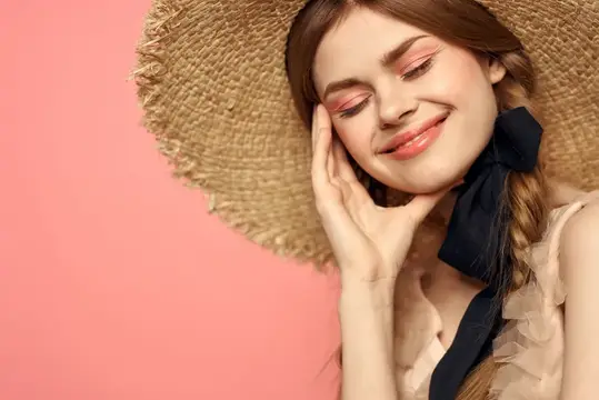 Улыбающаяся девушка в соломенной шляпе с чёрным бантом на розовом фоне