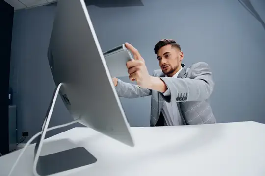 Мужчина в сером пиджаке фотографирует монитор на смартфон в офисе