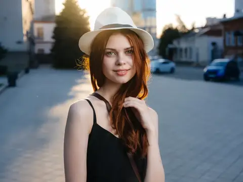 Модель с рыжими волосами на улице в городе, одетая в чёрное платье и белую шляпу