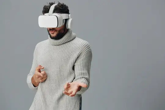 Бородатый мужчина в свитере и VR-очках на сером фоне