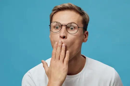 Удивлённый мужчина в очках прикрывает рот рукой на синем фоне