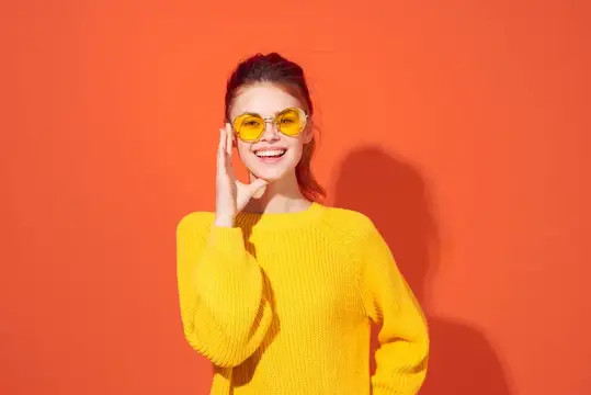 Улыбающаяся девушка в жёлтых очках на оранжевом фоне