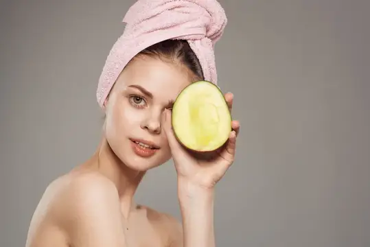 Улыбающаяся женщина с обнаженными плечами, с полотенцем на голове, держит в руке манго