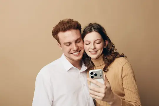 Улыбающаяся пара смотрит в смартфон на бежевом фоне