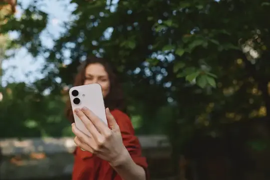 Девушка в красном платье фотографирует на смартфон в парке