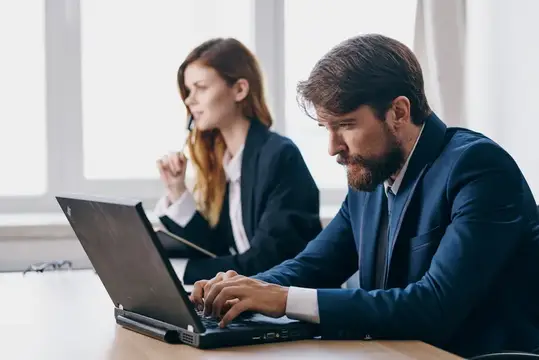 Сосредоточенный бородатый мужчина работает за ноутбуком в офисе