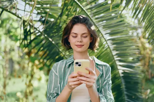Молодая женщина с телефоном в руках на фоне пальмовых листьев