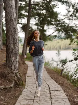 Спортивная женщина в повседневной спортивной одежде наслаждается пробежкой на свежем воздухе по живописному маршруту вдоль озера, что подчеркивает темы здоровья и хорошего самочувствия