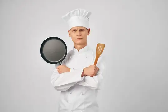Мужчина в поварской униформе, профессионально работающий с кухонными принадлежностями
