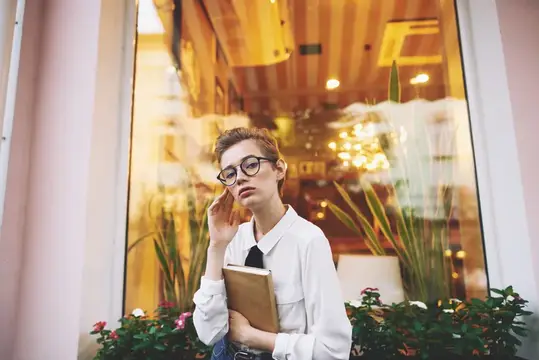 Молодая женщина в очках с книгой на фоне витрины кафе