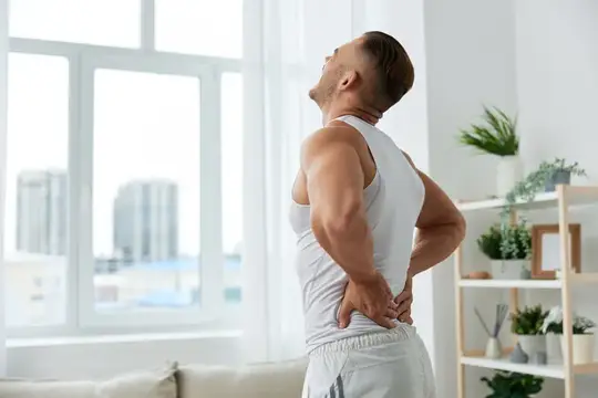 Мужчина испытывает боль в спине после тренировки дома, накачанный мужчина занимается спортом