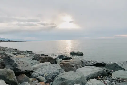 Каменистый берег моря под пасмурным небом с солнечным отблеском