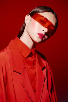 Бледная девушка в красных очках и костюме на алом фоне