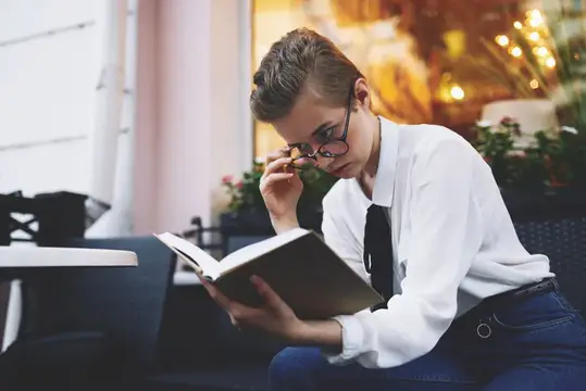 Молодой человек в очках увлечённо читает книгу в кафе