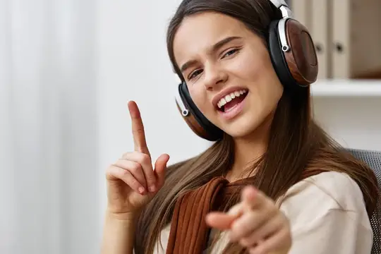 Улыбающаяся девушка в наушниках поёт и указывает пальцем вверх