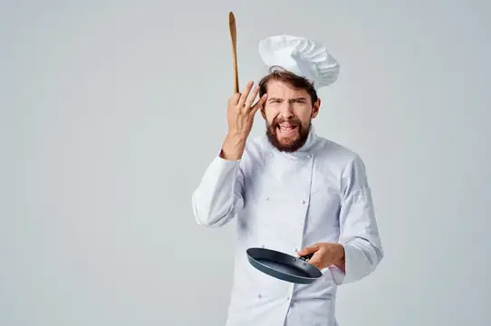 Раздражённый бородатый повар с деревянной ложкой и сковородой