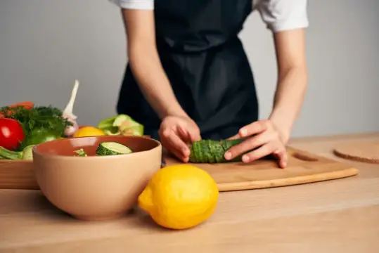 Домохозяйка в черном фартуке на кухне готовит витаминный салат