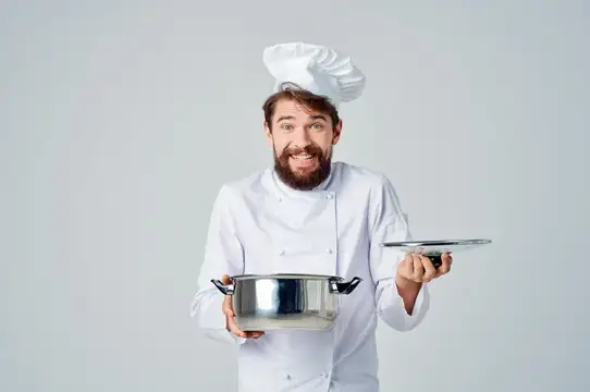 Улыбающийся бородатый повар с кастрюлей и крышкой на сером фоне