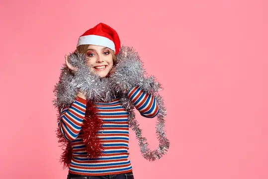 Улыбающаяся девушка в новогодней шапке с серебристой мишурой на розовом фоне