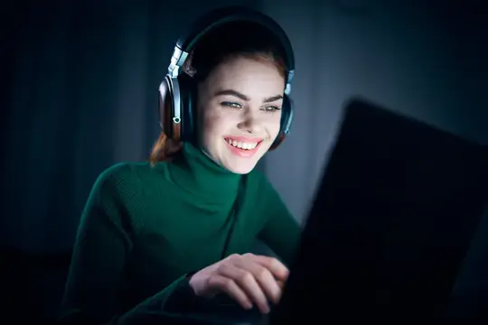 Женщина ночью сидит перед ноутбуком в наушниках, используя интернет-технологии